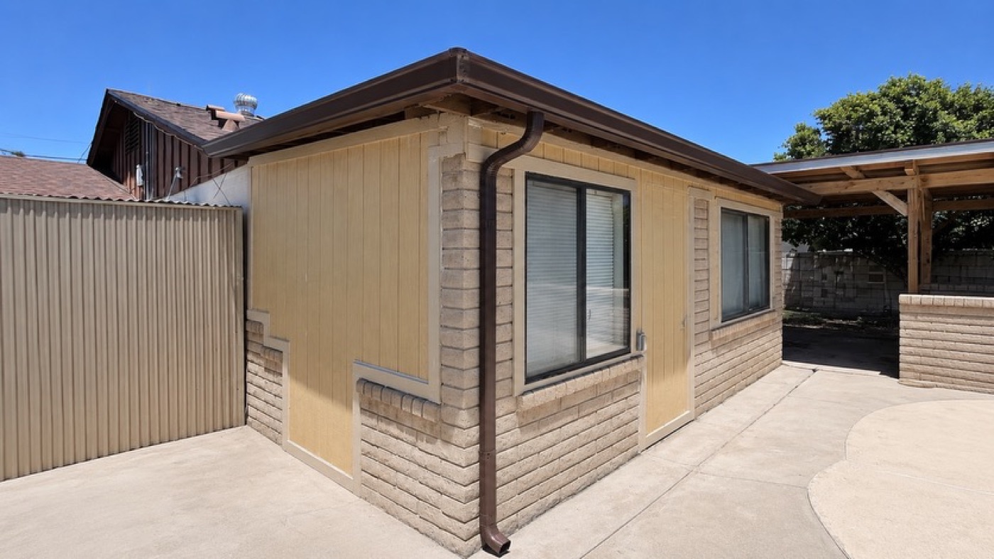 Brown seamless gutter and downspout on an older brick and board home with carport