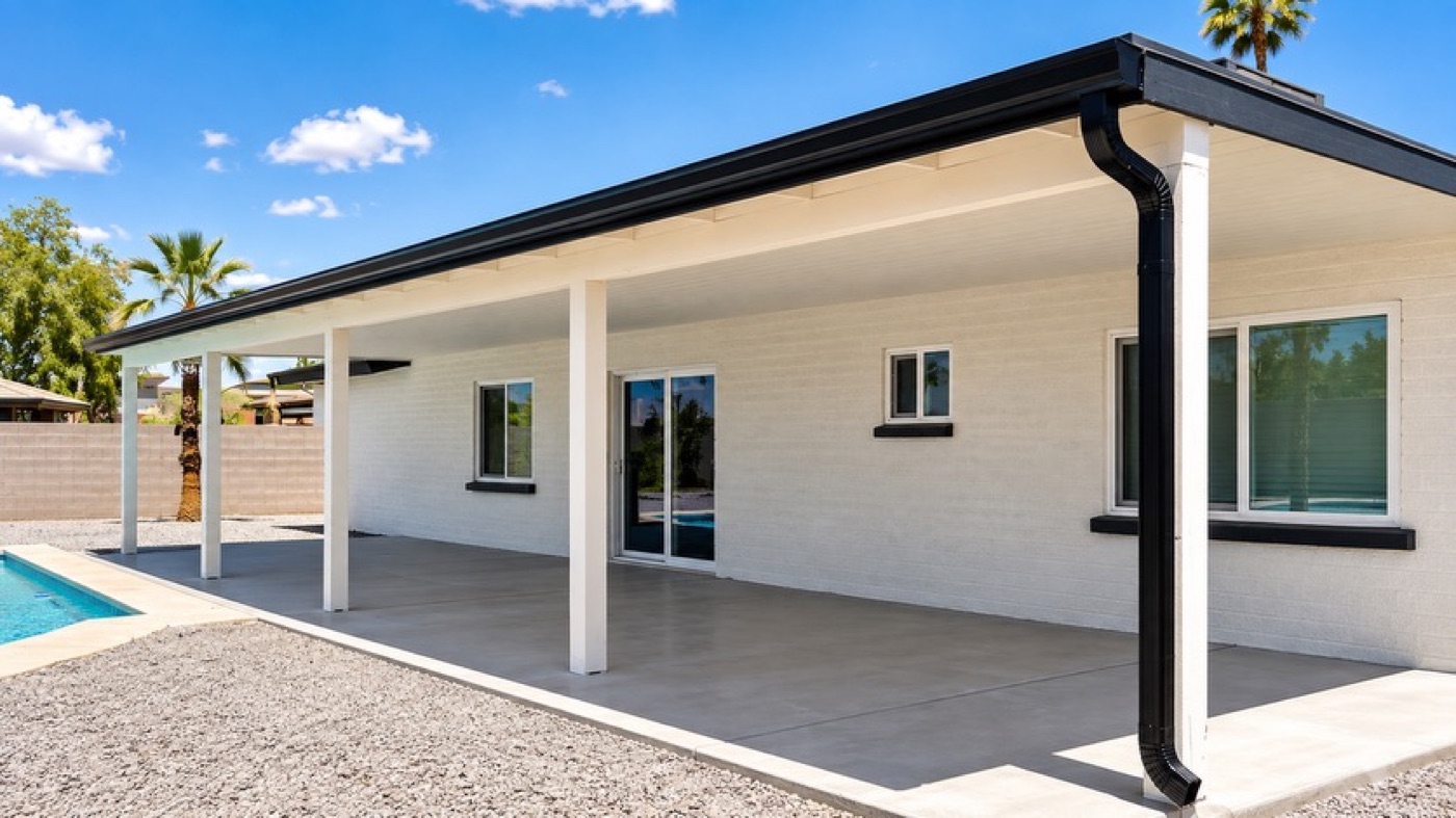 Black seamless gutter and downspout installed by Seamless Gutters on a white brick Phoenix home overlooking a pool