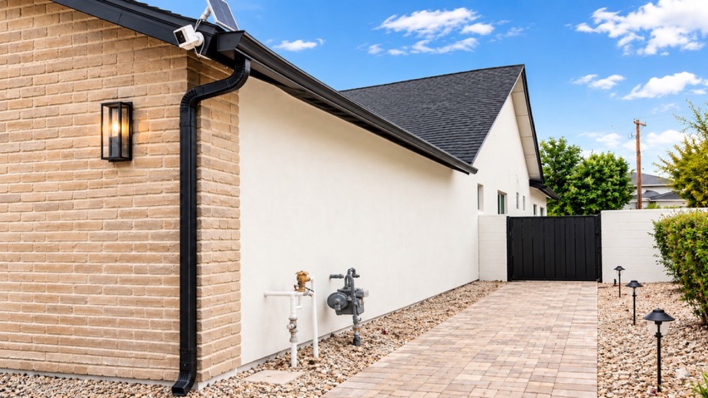 Black downspout running down a brick and stucco side elevation to a paver walkway