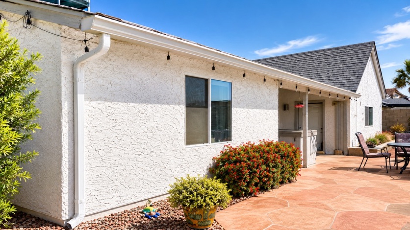 White seamless gutter and downspout on a white stucco home above a patio with planting